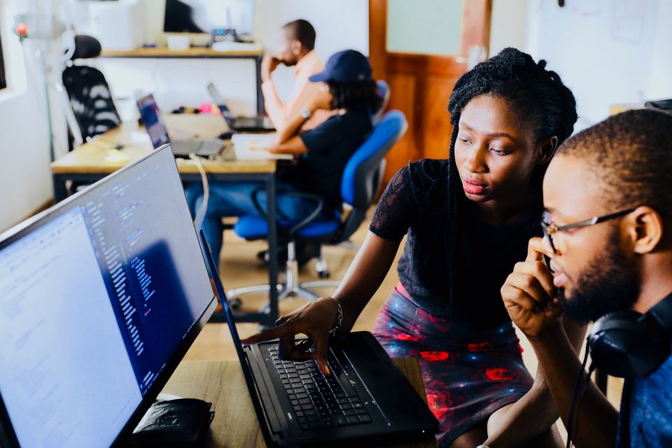 Photo shows two black people collaborating while looking at code in the foreground.  Photo by Mars on Unsplash.